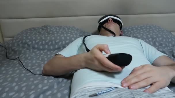 年轻的有魅力的男人使用眼睛按摩器装置 躺在床上 拿着遥控器 — 图库视频影像