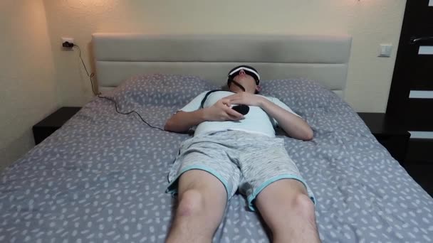 若い魅力的な男は リモート コントロールを押し ベッドに横たわって目マッサージ デバイスを使用してください — ストック動画