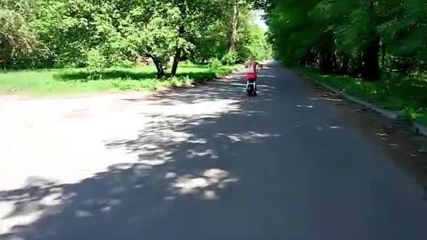 穿着红色礼服的年轻金发碧眼的女子在公园里骑电动摩托车时微笑着 — 图库视频影像