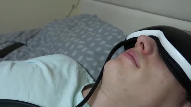 Joven Atractivo Hombre Utiliza Dispositivo Masajeador Ojos Acostado Cama Sosteniendo — Vídeos de Stock