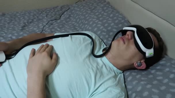 Joven Atractivo Hombre Utiliza Dispositivo Masajeador Ojos Acostado Cama Sosteniendo — Vídeos de Stock