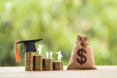 Siyah mezuniyet şapkası, şapka, öğrenci ve çocuk, yükselen bozuk paralar, masada beyaz saat, doğal yeşil arka plan. Devlet okulu finansmanı, eğitim fonu, mali konsept