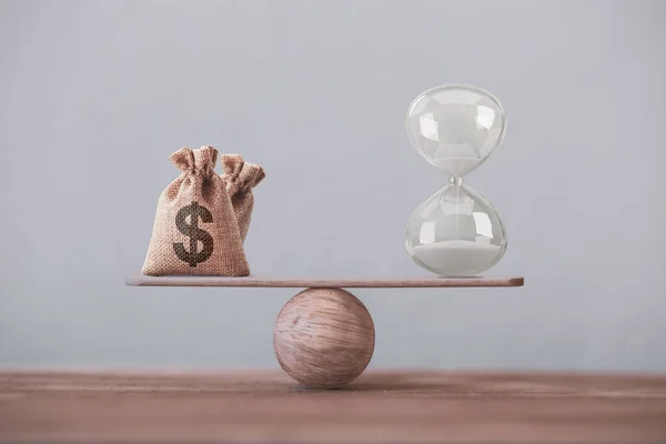 Kum saati ya da kum saati sembolü ve dolar çantasına eşit bir denge terazisi yazın. Finansal konsept: Paranın zaman değeri, zaman içinde varlık büyümesi, daha fazla para büyümesi için uzun vadeli sermayeye yapılan yatırımı resmediyor