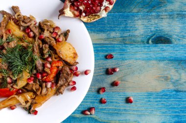 yeşil sebzeli fırında sığır eti, beyaz tabak mavi arka planda.