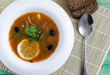 Beyaz bir tabakta et ve sebzeli çorba, arka planda hafif bir manzara.