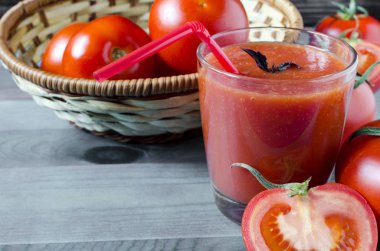 Ahşap arka planda domates suyu domatesleri ve fesleğen yapraklarıyla dolu bir bardak.