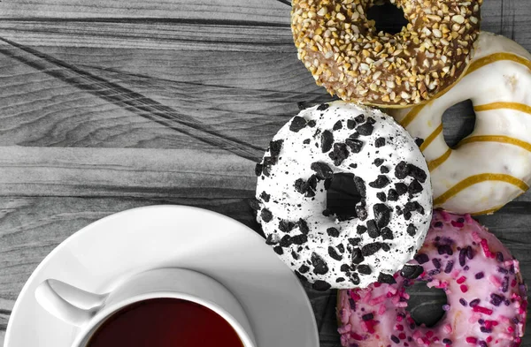 bright donuts in pink, white and brown colors and a white Cup of tea close-up black and white background place under the text