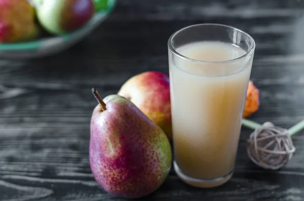 transparent glass of pear juice and juicy pears on a dark wooden background sharpness in the foreground