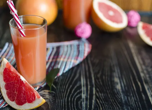 澄んだガラスの中に新鮮なグレープフルーツジュースと濃い木目の背景にグレープフルーツのスライスコピコスモス — ストック写真