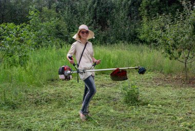 Çim kesme. İş elbiseleri kız bahçede çim mows. Büyük şapka ve gözlük kızı korumak. Kızlar kalıplaşmış değiştirme. Güçlü kadın kavramı. Bir biçme toplama sırasında gülümseyen kız