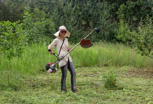 Çim kesme. İş elbiseleri kız bahçede çim mows. Büyük şapka ve gözlük kızı korumak. Kızlar kalıplaşmış değiştirme. Güçlü kadın kavramı. Bir biçme toplama sırasında gülümseyen kız