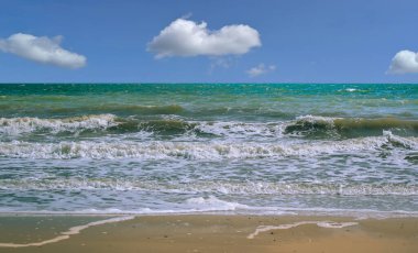 Fotoğrafta dar bir kum şeridi, dalgadan köpük, yeşilimsi su ve beyaz bulutlu mavi bir gökyüzü var. Karantina sırasındaki dinlenme. Boş alan.