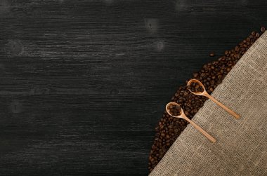 Kahve çekirdekleri içinde tahta kaşıklar çul çuval bezi üzerinde tuval ve kopya alanı bir siyah tablo yüzey zemin üzerine kahve dağınık.