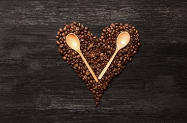 Kahve çekirdekleri kalp şekli formu ve tahta kaşıklar kopya alanı siyah ahşap yüzey zemin üzerine yaptı. Kahve kavramı sevgisi.