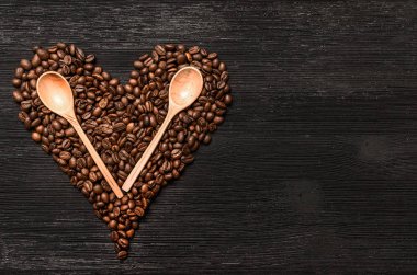 Kahve çekirdekleri kalp şekli formu ve tahta kaşıklar kopya alanı siyah ahşap yüzey zemin üzerine yaptı. Kahve kavramı sevgisi.