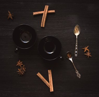 İki boş siyah çay Kupası ve Yıldız anason tarçın ve gümüş kaşık siyah ahşap masa arka plan üzerinde dizi.