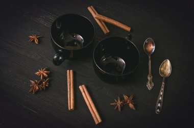 İki boş siyah çay Kupası ve Yıldız anason tarçın ve gümüş kaşık siyah ahşap masa arka plan üzerinde dizi.