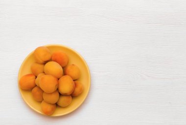 Beyaz ahşap masa arka plan kopya alanı ile izole sarı kase plaka üzerinde kayısı yığını.