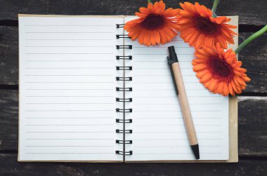 Ahşap arka plan boş sayfa Not defteri ve turuncu gerbera çiçekleri.