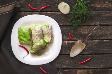 Lahana rulo beyaz tabakta. Çiğ kıyılmış domuz ile sığır yeşil lahana yaprakları, kırmızı biber biber ve yeşil dereotu.