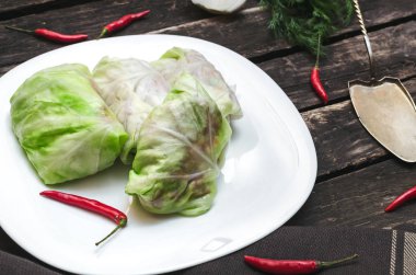 Lahana rulo beyaz tabakta. Çiğ kıyılmış domuz ile sığır yeşil lahana yaprakları, kırmızı biber biber ve yeşil dereotu.