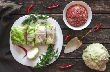 Lahana rulo beyaz tabakta. Çiğ kıyılmış domuz ile sığır yeşil lahana yaprakları, kırmızı biber biber ve yeşil dereotu.