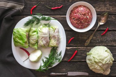 Lahana rulo beyaz tabakta. Çiğ kıyılmış domuz ile sığır yeşil lahana yaprakları, kırmızı biber biber ve yeşil dereotu.