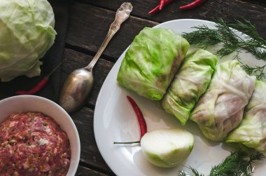 Lahana rulo beyaz tabakta. Çiğ kıyılmış domuz ile sığır yeşil lahana yaprakları, kırmızı biber biber ve yeşil dereotu.