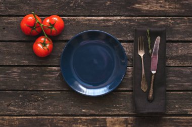 Kopya alanı, kırmızı tomate ve çatal bıçak mutfak masa arka plan üzerinde ile dalı ile boş mavi tabak.