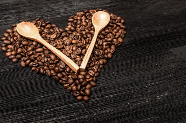 Kahve çekirdekleri kalp şekli formu ve tahta kaşıklar kopya alanı siyah ahşap yüzey zemin üzerine yaptı. Kahve kavramı sevgisi.