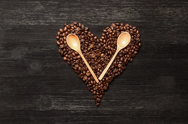 Kahve çekirdekleri kalp şekli formu ve tahta kaşıklar kopya alanı siyah ahşap yüzey zemin üzerine yaptı. Kahve kavramı sevgisi.