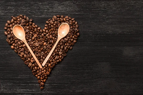Kahve çekirdekleri kalp şekli formu ve tahta kaşıklar kopya alanı siyah ahşap yüzey zemin üzerine yaptı. Kahve kavramı sevgisi.