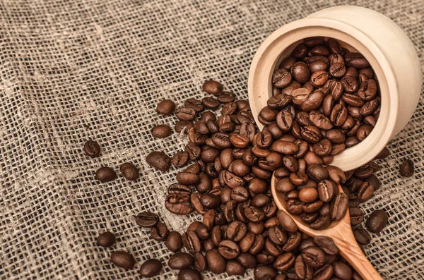 stock image Coffee beans scattered from a wooden pot and wood spoon on burlap cloth background. Close up photo.