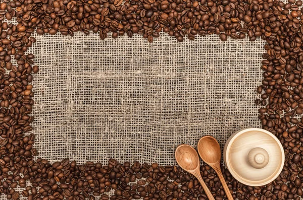 Coffee beans frame border with copy space in the center on burlap cloth background.