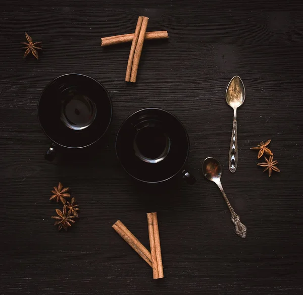 İki boş siyah çay Kupası ve Yıldız anason tarçın ve gümüş kaşık siyah ahşap masa arka plan üzerinde dizi.
