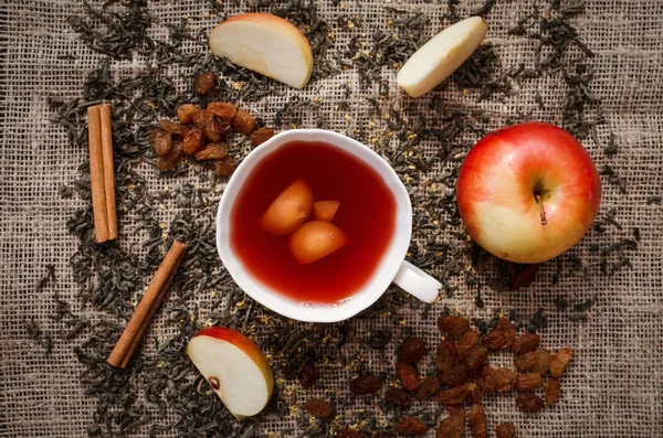 Cup of stewed fruit compote drink with scattered ingredients around on burlap cloth background.