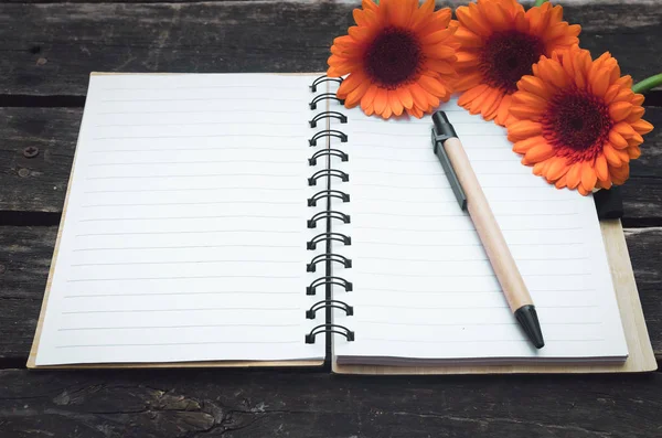 Ahşap arka plan boş sayfa Not defteri ve turuncu gerbera çiçekleri.