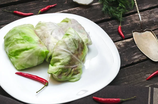 Lahana rulo beyaz tabakta. Çiğ kıyılmış domuz ile sığır yeşil lahana yaprakları, kırmızı biber biber ve yeşil dereotu.
