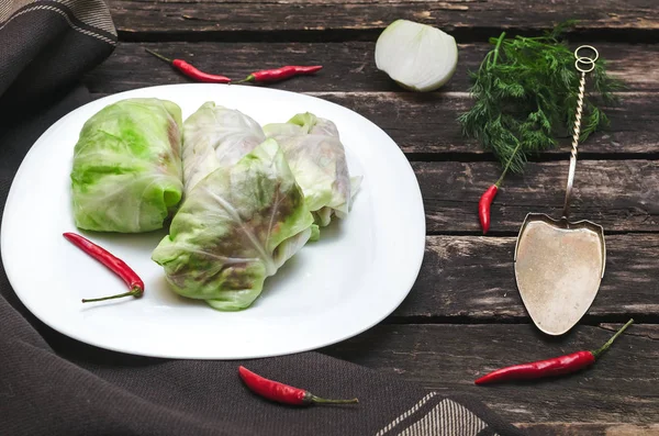 Lahana rulo beyaz tabakta. Çiğ kıyılmış domuz ile sığır yeşil lahana yaprakları, kırmızı biber biber ve yeşil dereotu.