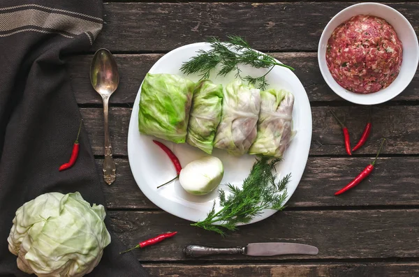 Lahana rulo beyaz tabakta. Çiğ kıyılmış domuz ile sığır yeşil lahana yaprakları, kırmızı biber biber ve yeşil dereotu.
