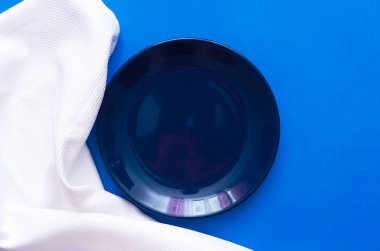 Mavi mutfak masasının üzerine beyaz yemek kumaş ve boş levha.