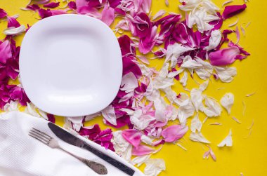 Boş tabak, çanak bez, çatal ve bıçak peony çiçek yaprakları tablo arka plan ile dağınık. Romantik yemek kavramı.