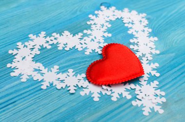 Beyaz kar taneleri ve mavi ahşap tahta arka plan üzerinde kırmızı kalp kalp şekli yapılır.