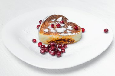 Beyaz ahşap masa arka plan üzerinde kızılcık ve pudra şekeri ile plaka üzerinde taze pişmiş kalp şekli lor.