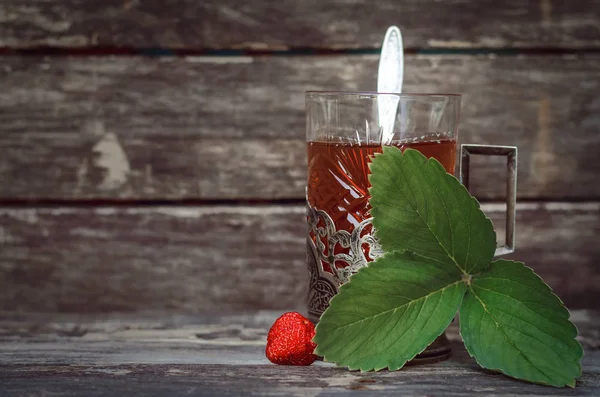 Green tea with strawberry leaves on wooden table background.