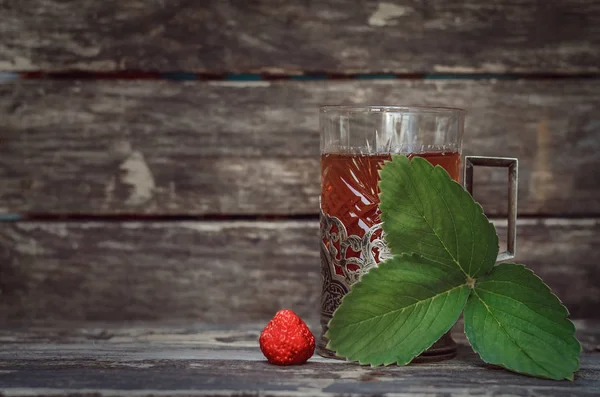 Green tea with strawberry leaves on wooden table background.