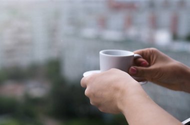 Kadın bir fincan kahve ve şehre aşağıdaki pencereden bakıyor tutuyor.