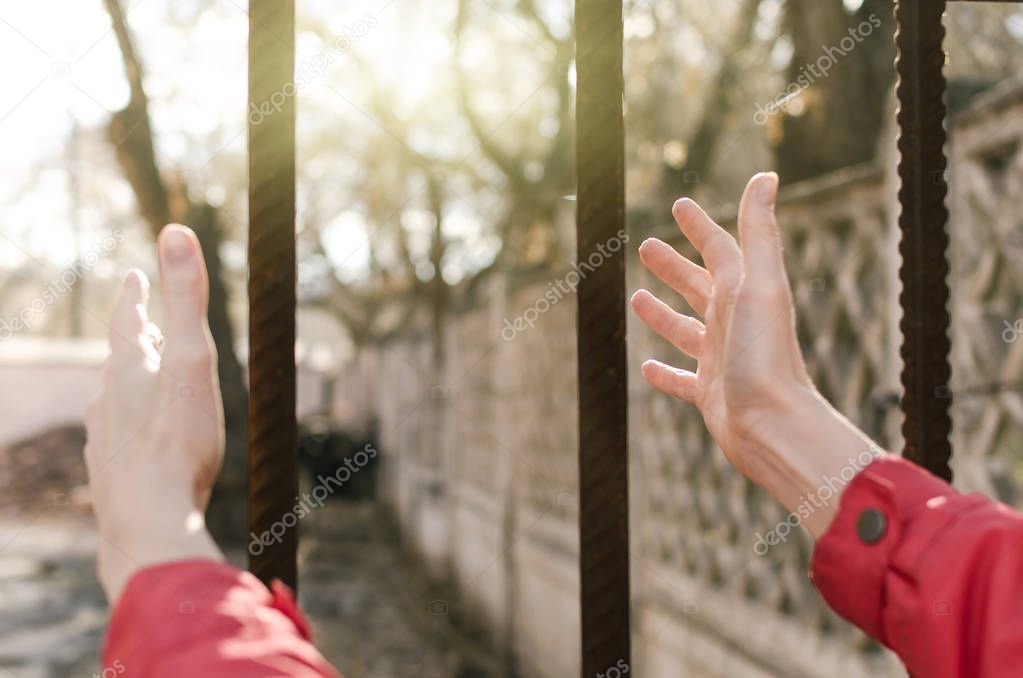 Woman pulls her hands through the bars to the sun. Female freedom concept.