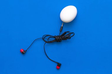 Tavuk yumurta kulaklık beden ile mavi arka plan üzerinde yürüyor.