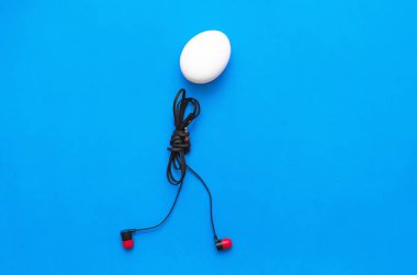 Tavuk yumurta kulaklık beden ile mavi arka plan üzerinde yürüyor.